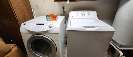 A laundry area with a front-loading washing machine and a dryer. There is a cardboard box on the dryer and a small orange umbrella hanging on the wall.
