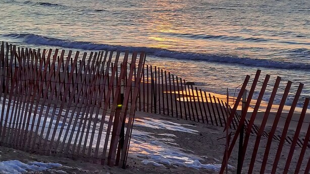 Una spiaggia con una recinzione di legno e onde.