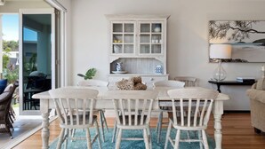 A dining area with a white table and chairs, a cabinet with glass doors, and a painting on the wall.