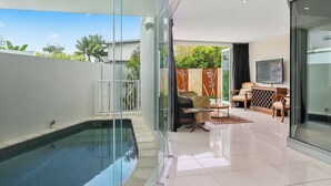 A modern indoor pool area with a glass enclosure, a seating area with a sofa and chairs, and a television on the wall.