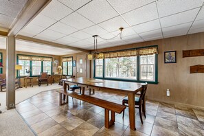 Enjoy meals and gatherings in this spacious dining area with a large table and benches, surrounded by artwork and a view of the outdoors.