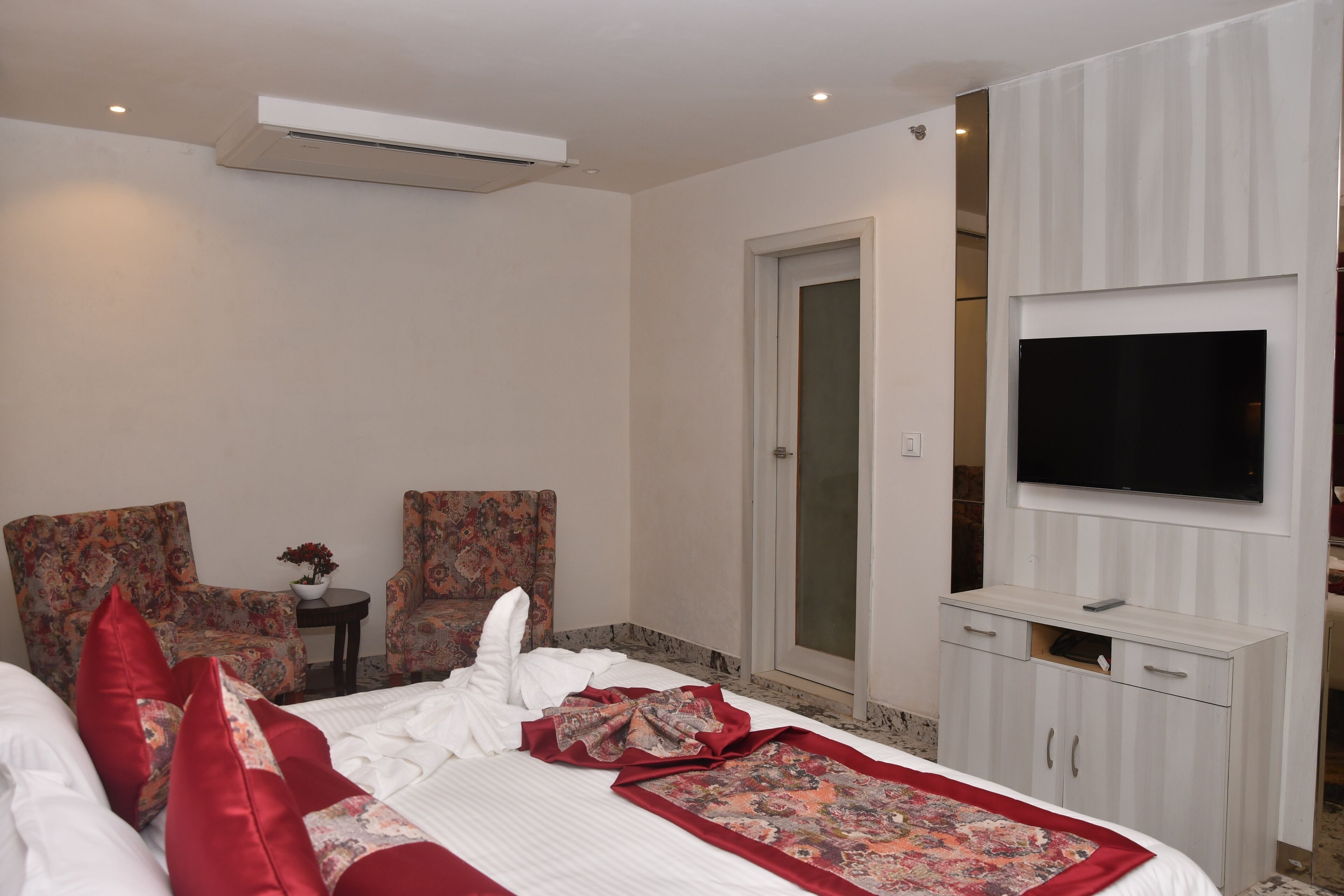 Een hotelkamer met een bed, twee fauteuils, een tafeltje met een vaas, een televisie op een kast en een deur.