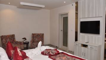 Een hotelkamer met een bed, twee fauteuils, een tafeltje met een vaas, een televisie op een kast en een deur.