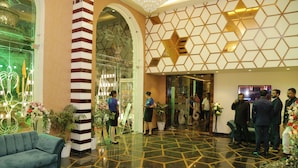 A hotel lobby with a geometric floor pattern, a blue sofa, and a reception area with staff. - Lotus Ananta Elite Kota (Kota)