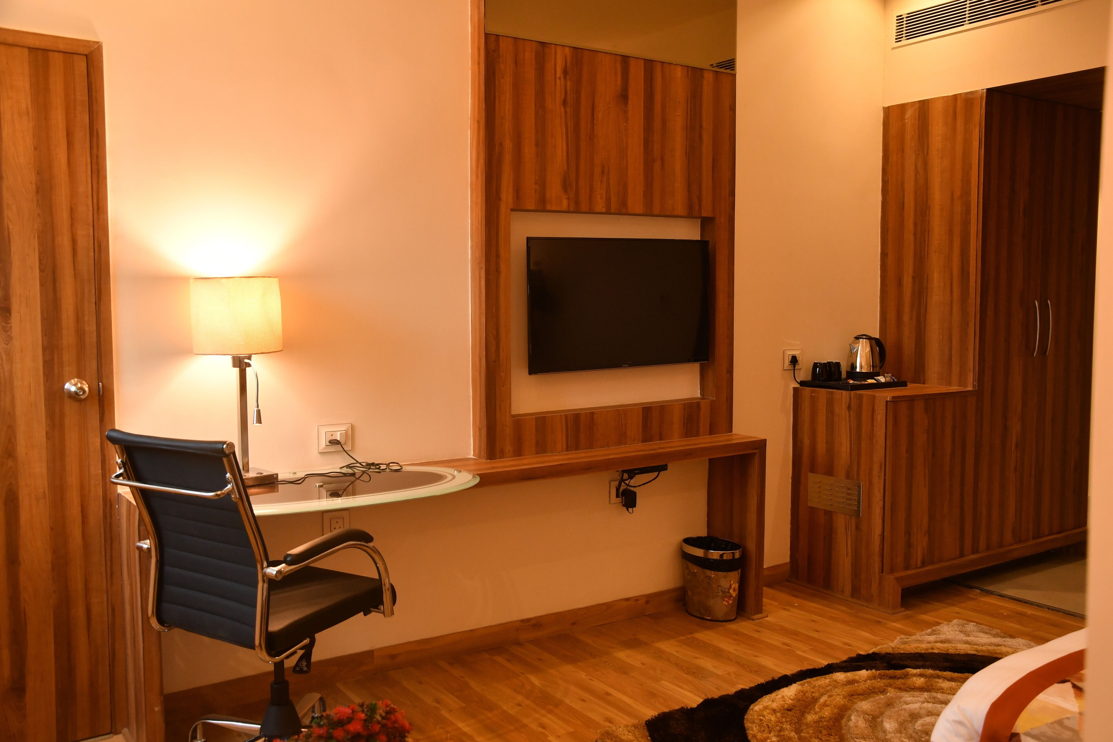 A bathroom with a wooden vanity, a sink, a mirror, a television mounted above the mirror, a chair, and a trash bin.