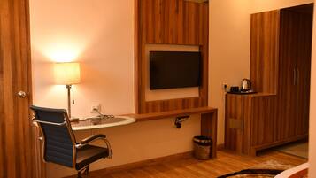A bathroom with a wooden vanity, a sink, a mirror, a television mounted above the mirror, a chair, and a trash bin.