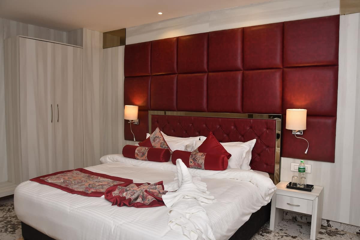 A hotel room with a large bed, a red headboard, two bedside lamps, a nightstand with a phone and a bottle, and a wardrobe.