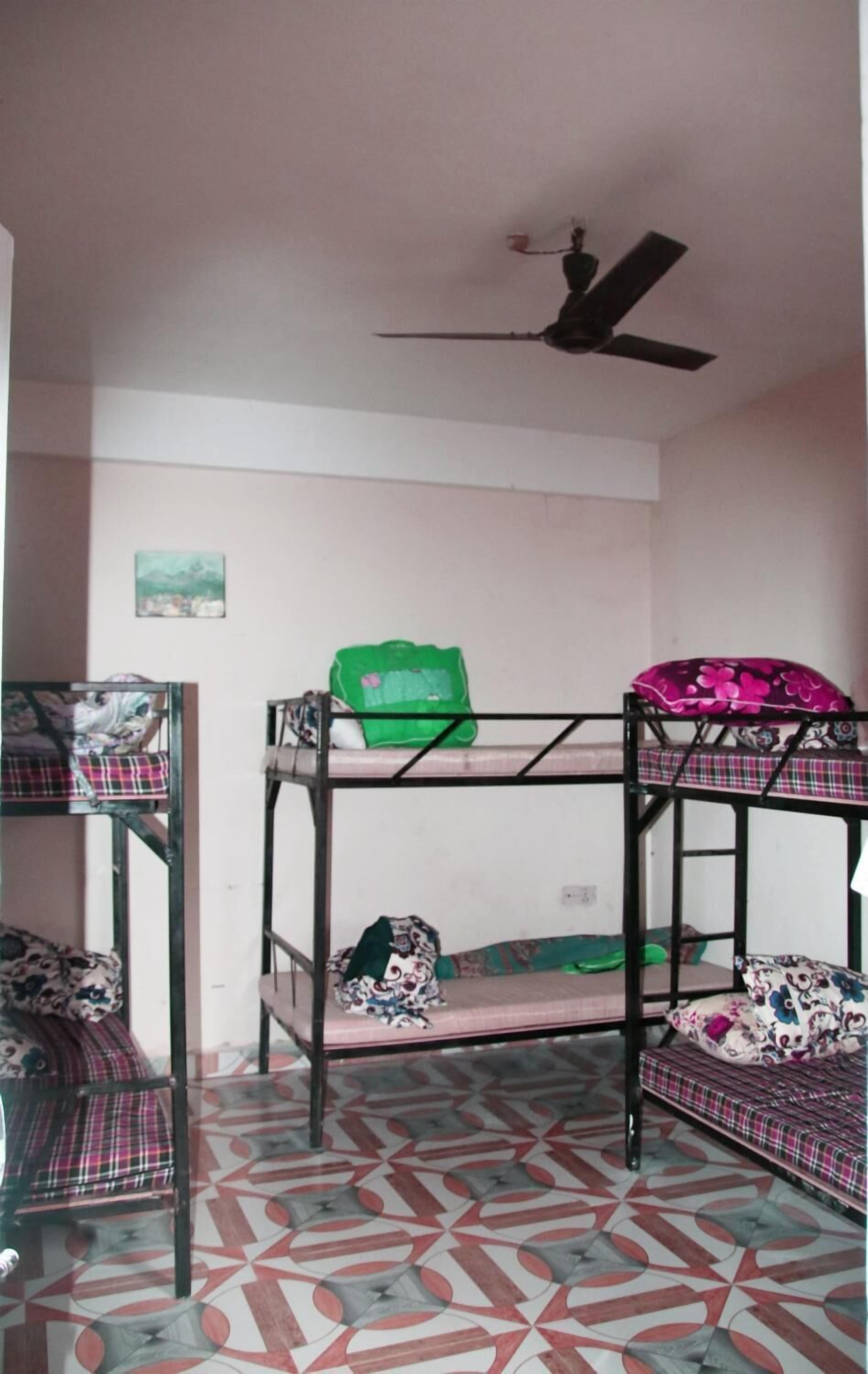 A dormitory room with bunk beds, a ceiling fan, and patterned floor tiles.