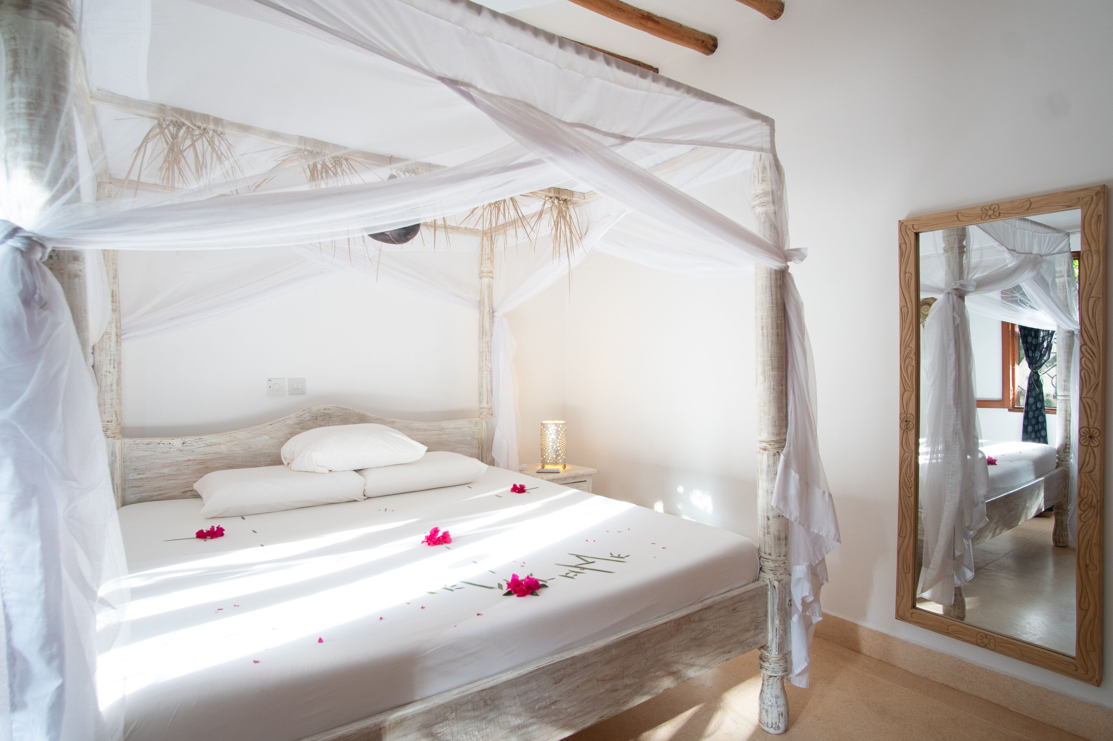 Un lit à baldaquin, une lampe de chevet et un miroir au mur.