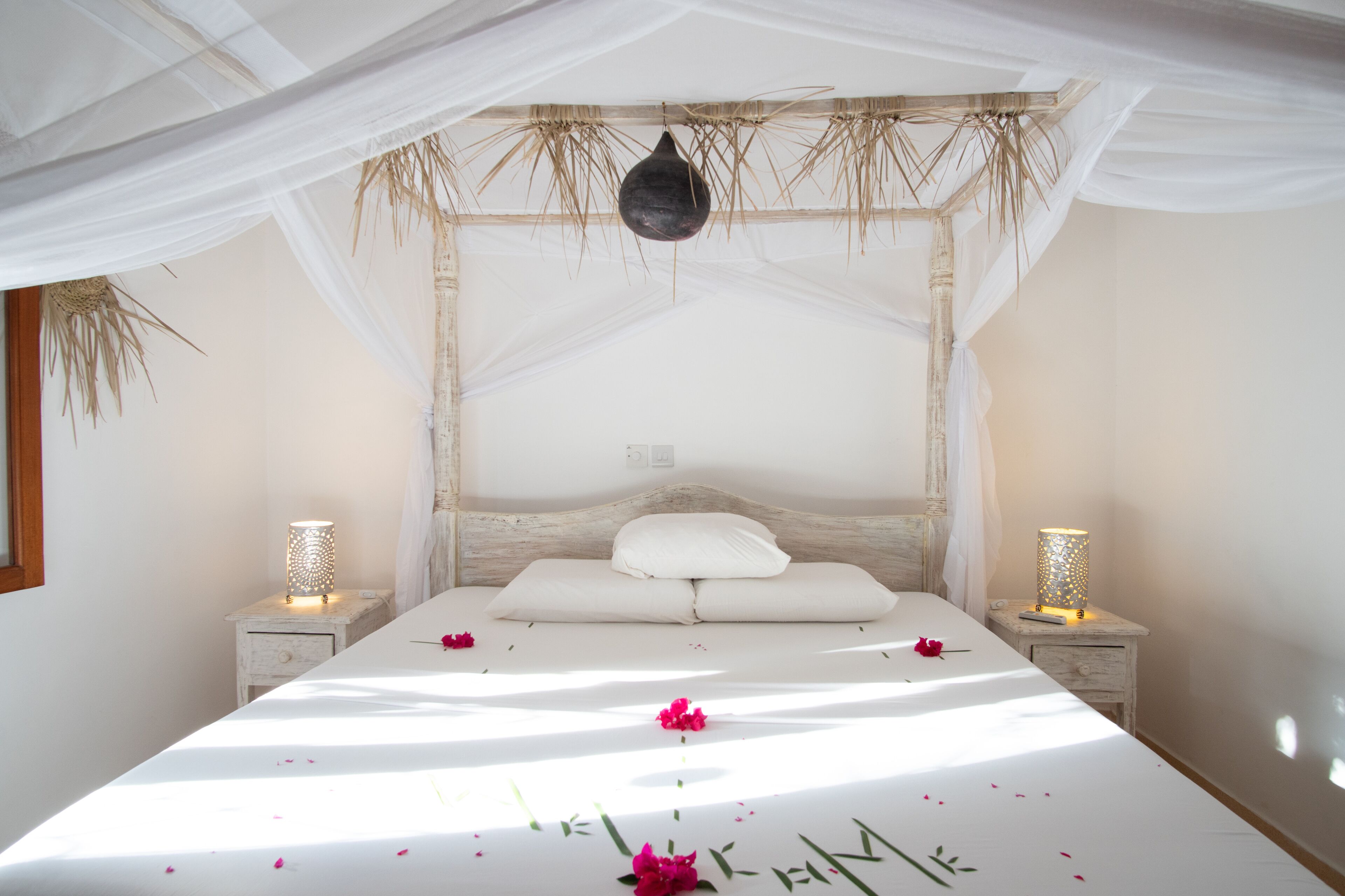A bed with a canopy, two bedside lamps, and a decorative hanging object.