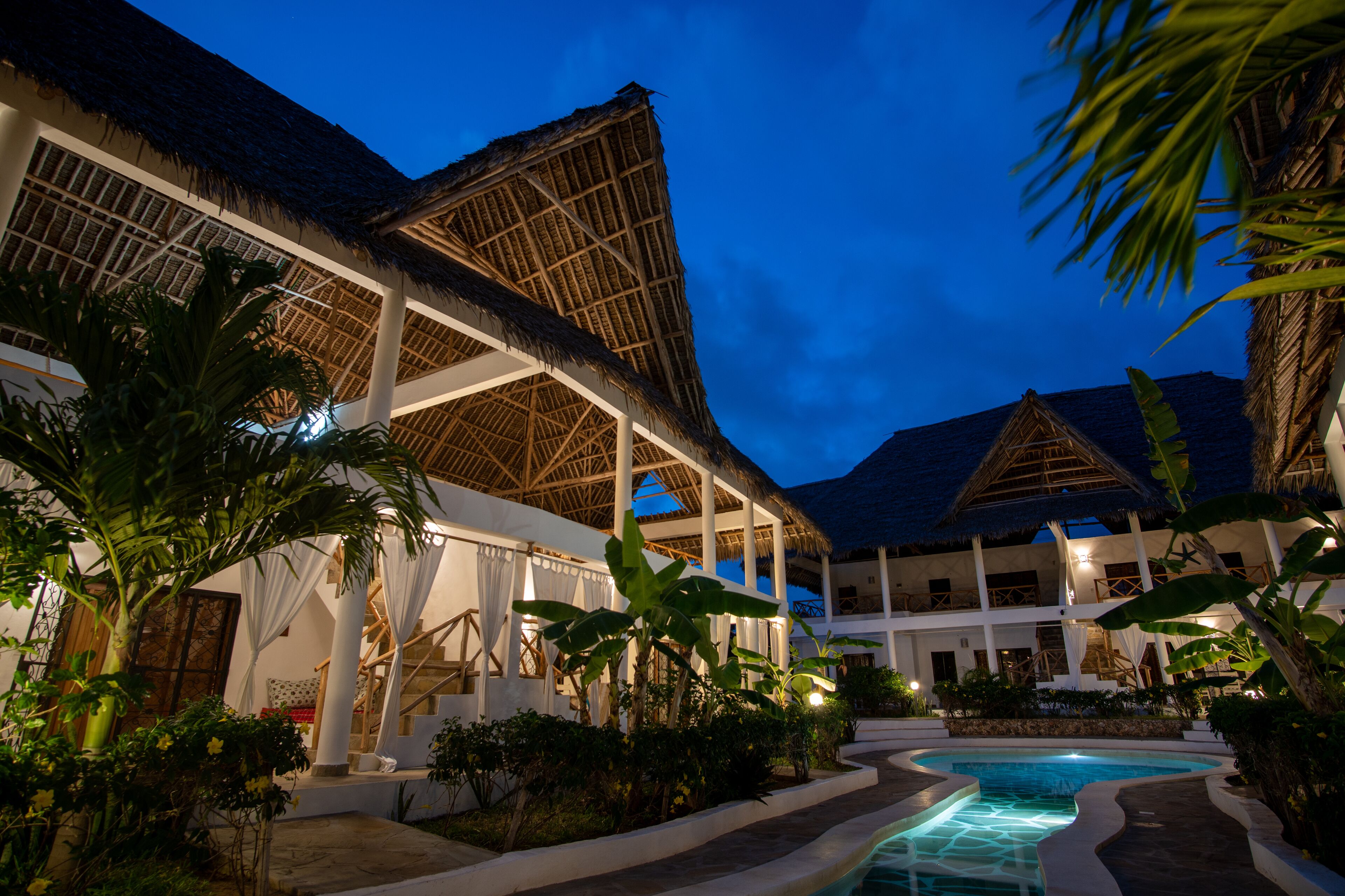 A resort with a swimming pool, thatched-roof structures, and lush greenery.