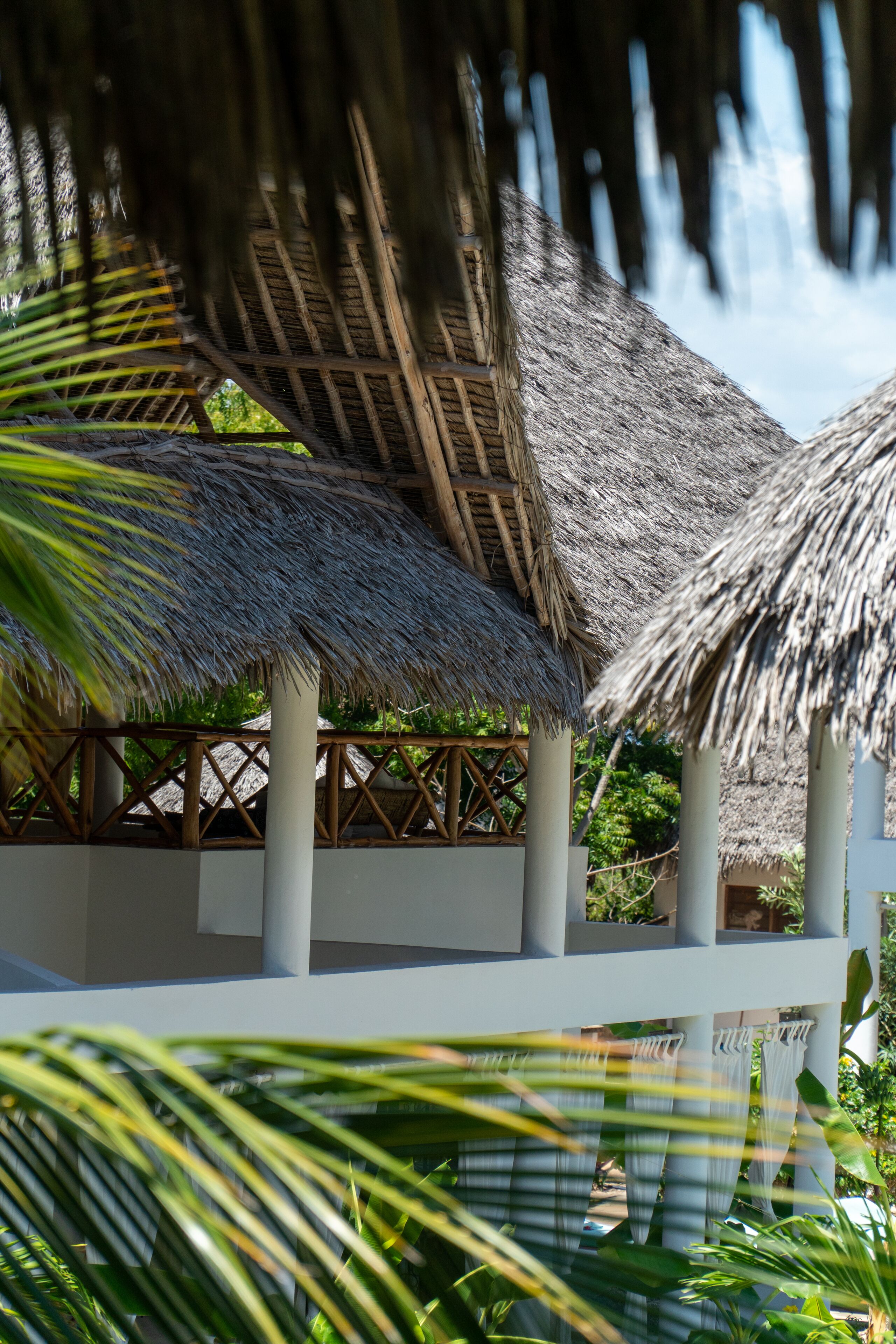 A thatched-roof structure with a wooden lattice design, surrounded by lush greenery.