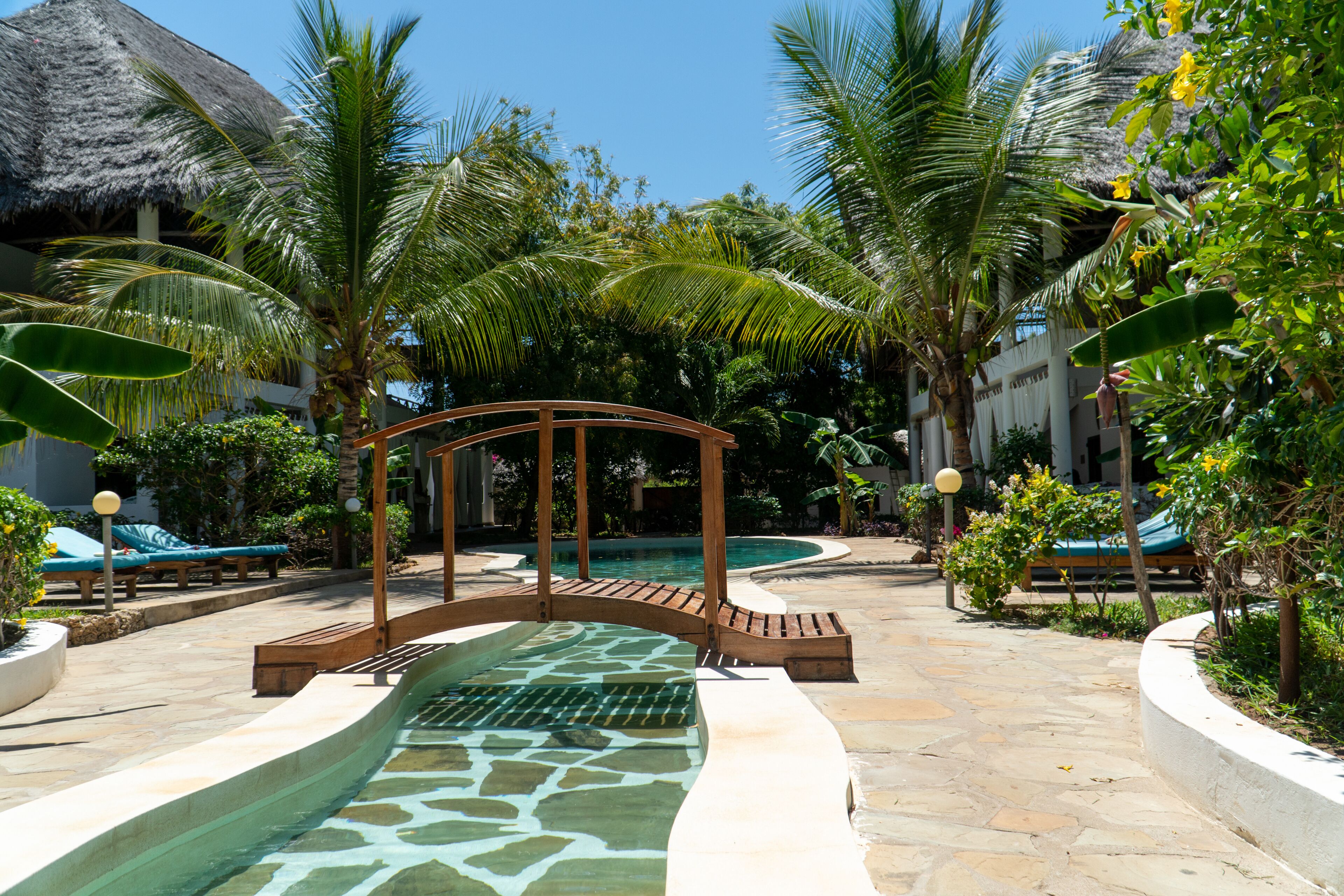 A pool area with a wooden gazebo, lounge chairs, and palm trees.