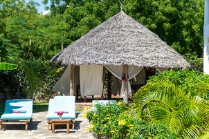 A thatched-roof hut with two lounge chairs and a small table with a flower vase.