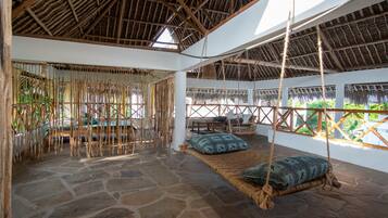 A room with a stone floor, thatched roof, and a hanging swing with cushions.