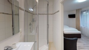 Uma casa de banho moderna com cabine de duche em vidro, lavatório branco e espelho grande.