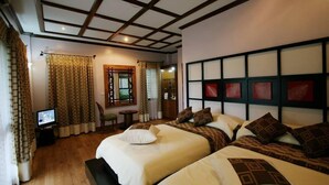 A hotel room with two beds, a television, a small table, and a window with curtains.