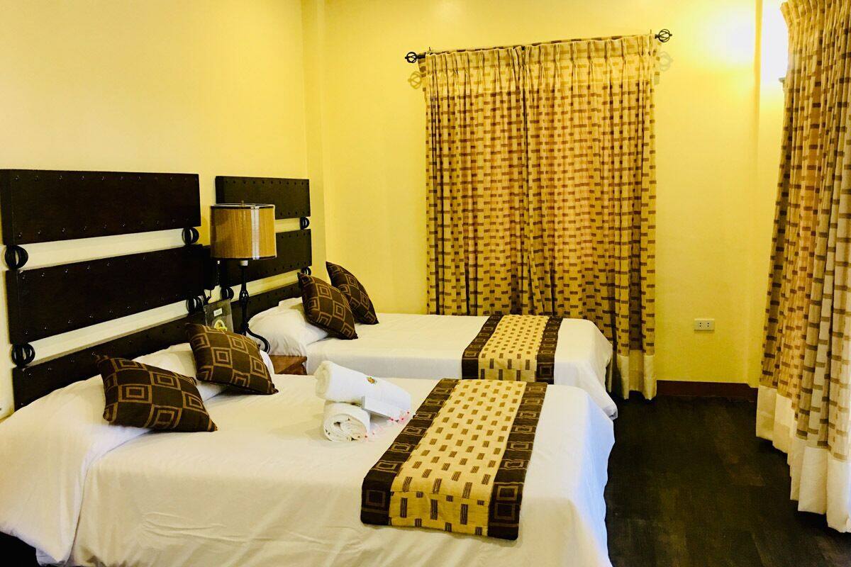 Una habitación de hotel con dos camas, un cabecero, una lámpara y cortinas estampadas.