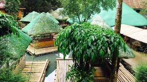 A bamboo raft on a river surrounded by thatched-roof huts.