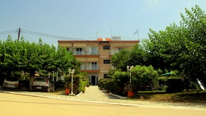 A two-story building with a tiled roof and a flag on top. There are potted plants and a pathway leading to the entrance. - Giota Rooms (Pineios)