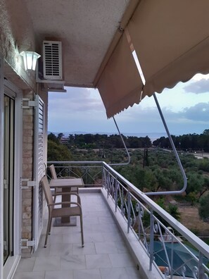 Un balcón con mesa y sillas, un equipo de aire acondicionado y vistas a un paisaje verde.