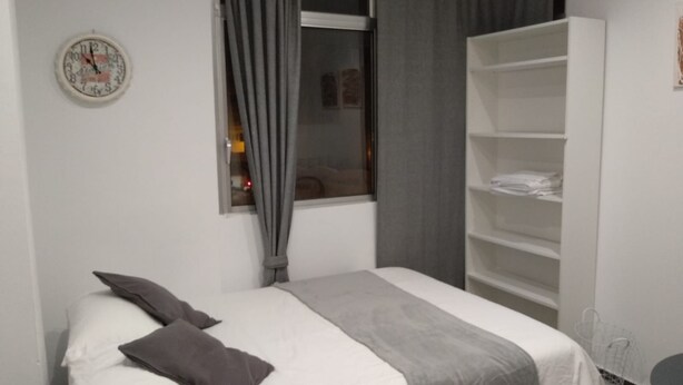 A bedroom with a bed, a window with curtains, a white wardrobe, and a wall clock. - Residencial Fontanillo (Las Palmas de Gran Canaria)