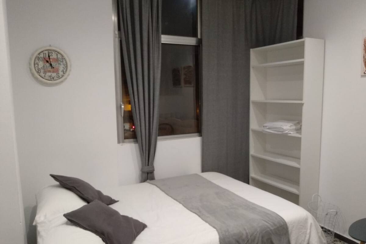 Un dormitorio con cama, una ventana con cortinas, un armario blanco y un reloj de pared.