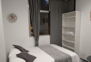 Un dormitorio con cama, una ventana con cortinas, un armario blanco y un reloj de pared.