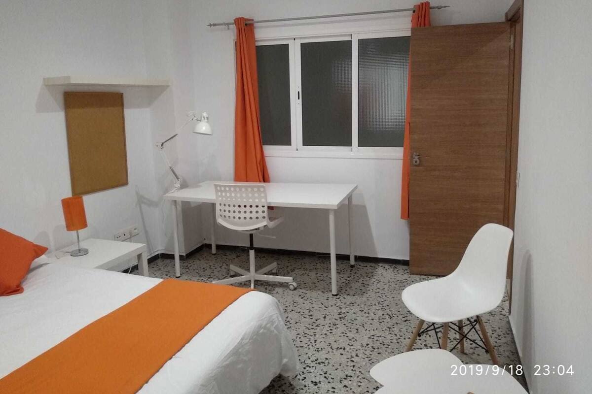 Una habitación de hotel con cama, escritorio, silla, ventana con cortinas y puerta.