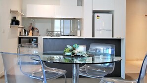Une cuisine moderne avec des meubles blancs, une table à manger en verre et des chaises transparentes.