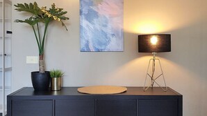 Une pièce moderne avec un meuble de couleur sombre, une plante en pot, une lampe et deux tableaux abstraits accrochés au mur.