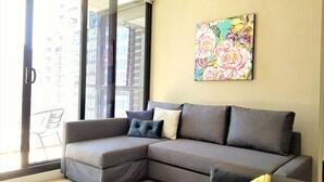 Un salon moderne avec un canapé d’angle gris, une table basse noire et un tableau floral aux couleurs vives accroché au mur.