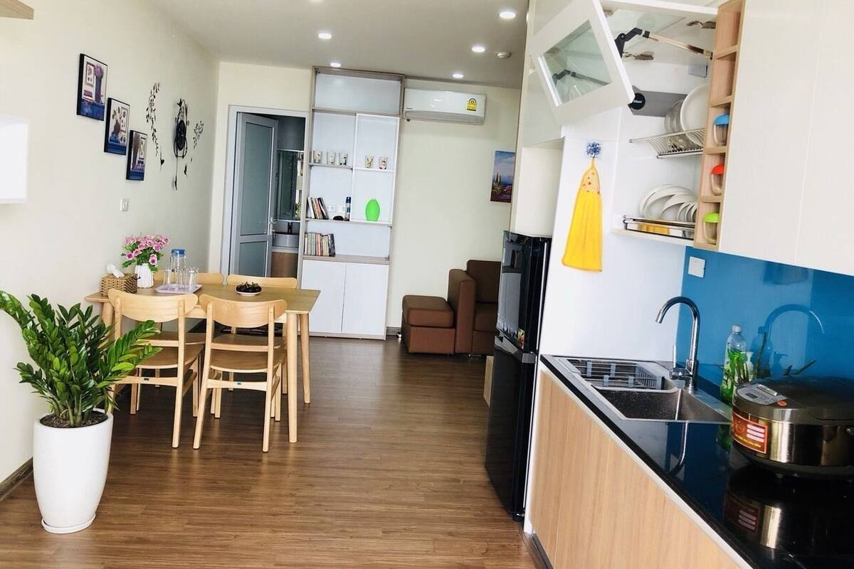 A modern kitchen with a built-in oven, a sink, and a microwave. There is a dining area with a table and chairs, and a potted plant.