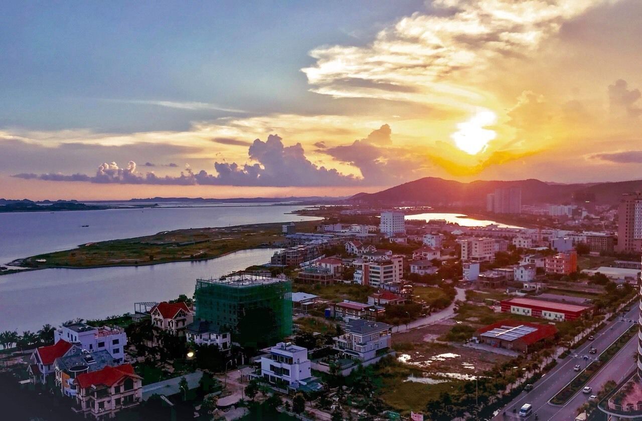 A coastal cityscape with buildings, a body of water, and a sunset.