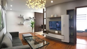 A modern living room with a sofa, glass coffee table, and a flat-screen TV mounted on a wall. - Zan- Newlife Halong Apartment (Bai Chay)
