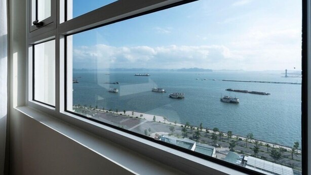 A view from a window overlooking a body of water with several ships and a distant bridge. - Zan- Newlife Halong Apartment (Bai Chay)