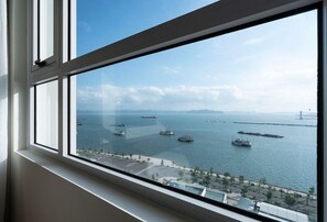A view from a window overlooking a body of water with several ships and a distant bridge. - Zan- Newlife Halong Apartment (Bai Chay)