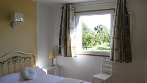 Ein Schlafzimmer mit Bett, Stuhl, einem Fenster mit Vorhängen, einem Nachttisch mit Lampe und einer Wanduhr.