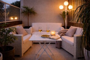Een terras met een witte tafel, twee witte banken, een bloempot en een kaars.