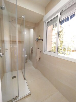 A modern bathroom with a glass shower enclosure, a toilet, and a window providing a view of the outdoors.