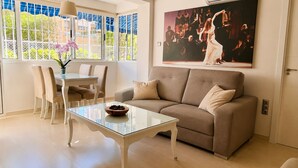 Una sala de estar con una mesa de centro de vidrio, sofá color beige y una zona de comedor con sillas y una mesa.