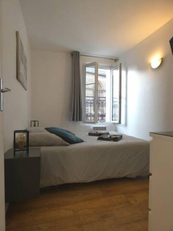 A bedroom with a bed, bedside table, and a window with curtains.