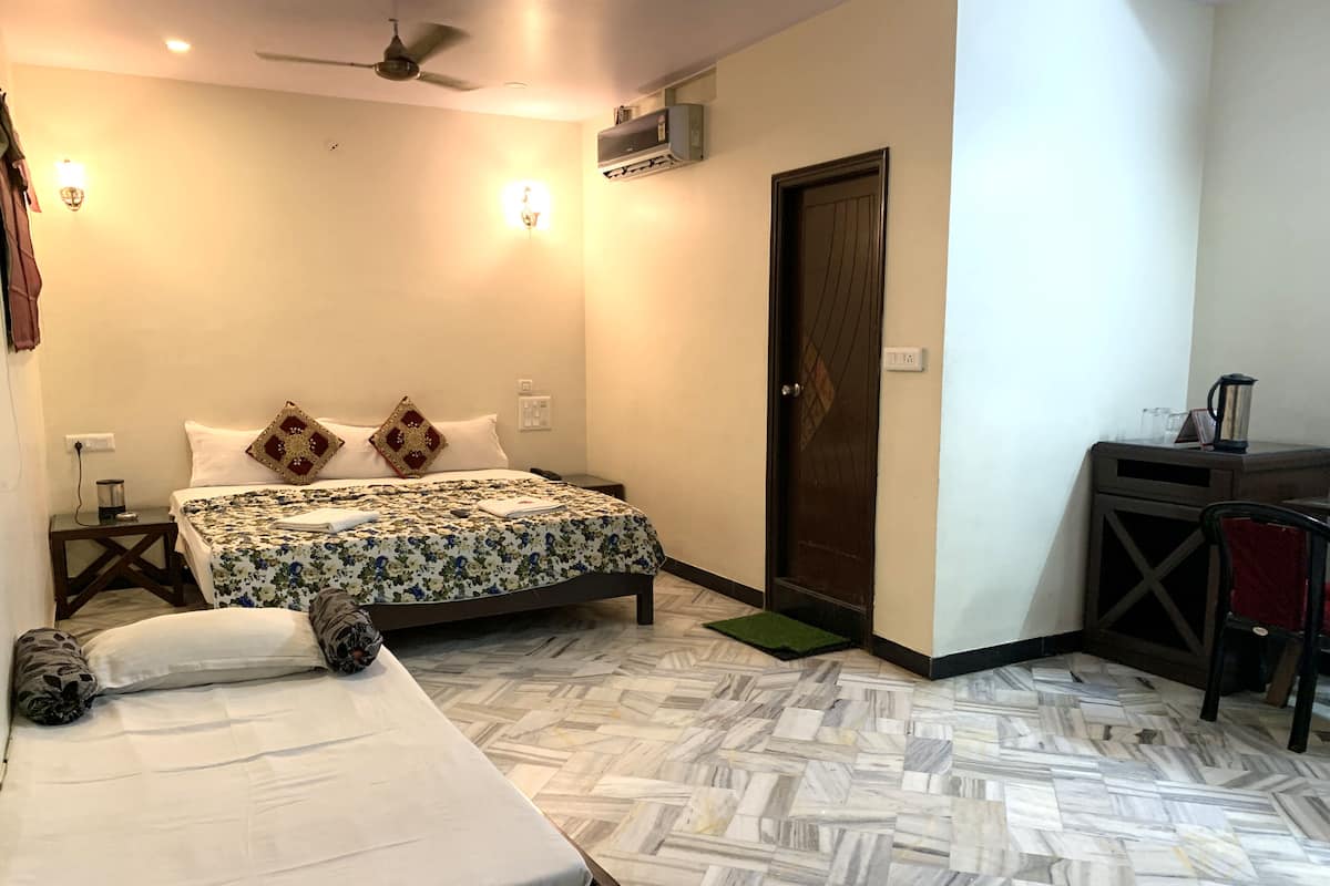 Quarto de hotel com cama, uma cama adicional, escrivaninha, cadeira, aquecedor e porta.