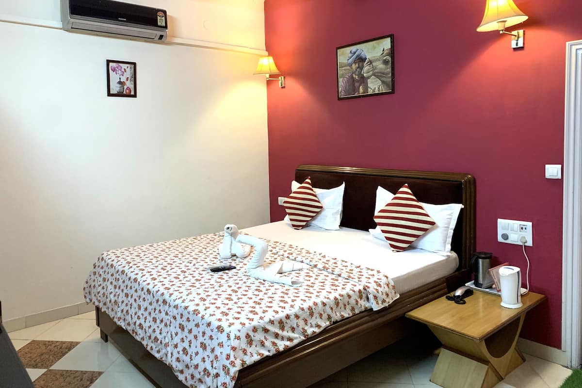 Quarto de hotel com cama, mesas de cabeceira, ar condicionado, um quadro e uma luminária.