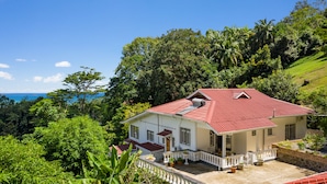 Ein weißes Haus mit rotem Dach, umgeben von üppigem Grün und Blick aufs Meer.