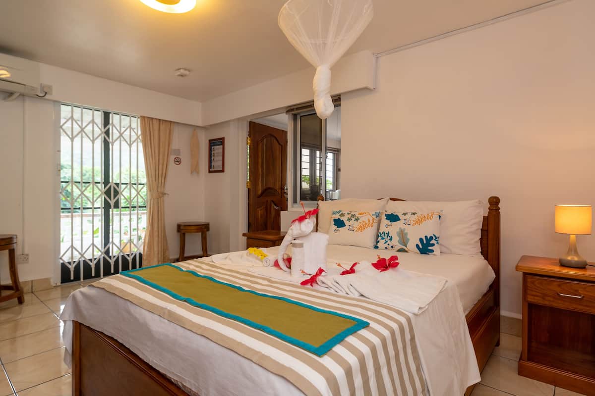 Hotelkamer met een bed, nachtkastje, raam met gordijnen, een deur en een klamboe boven het bed.