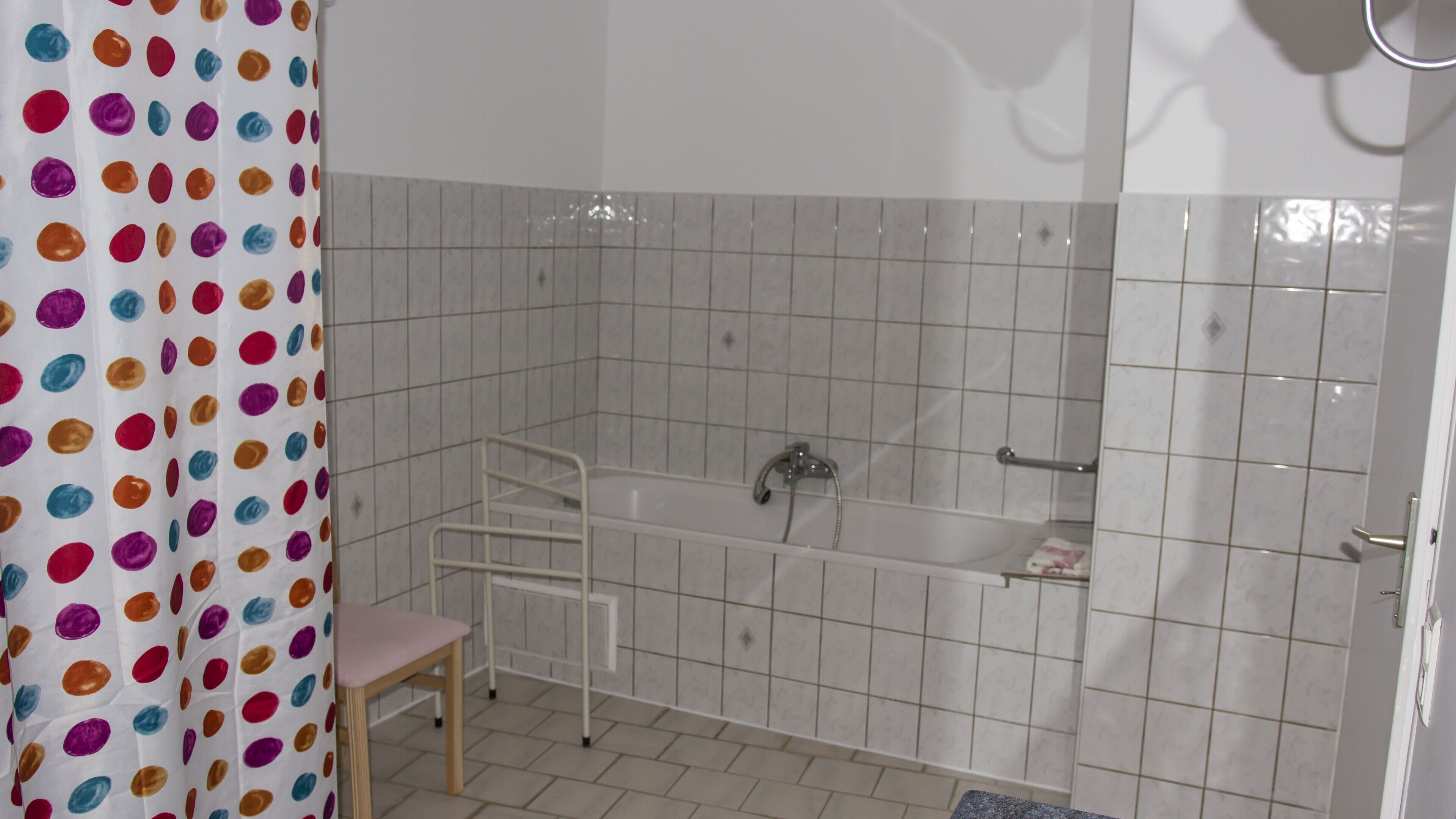 Baño con una bañera blanca, ducha e inodoro. Hay una silla y un perchero para toallas.