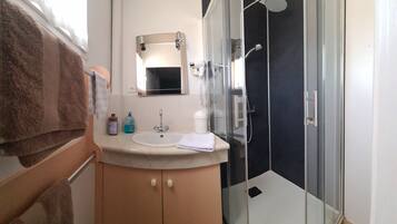 A modern bathroom with a glass shower enclosure, a sink with a mirror above, and toiletries on the countertop.