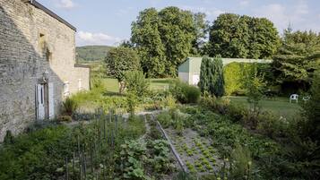 Ein rustikales Steinhaus mit Garten, umgeben von Bäumen und einem grünen Feld.