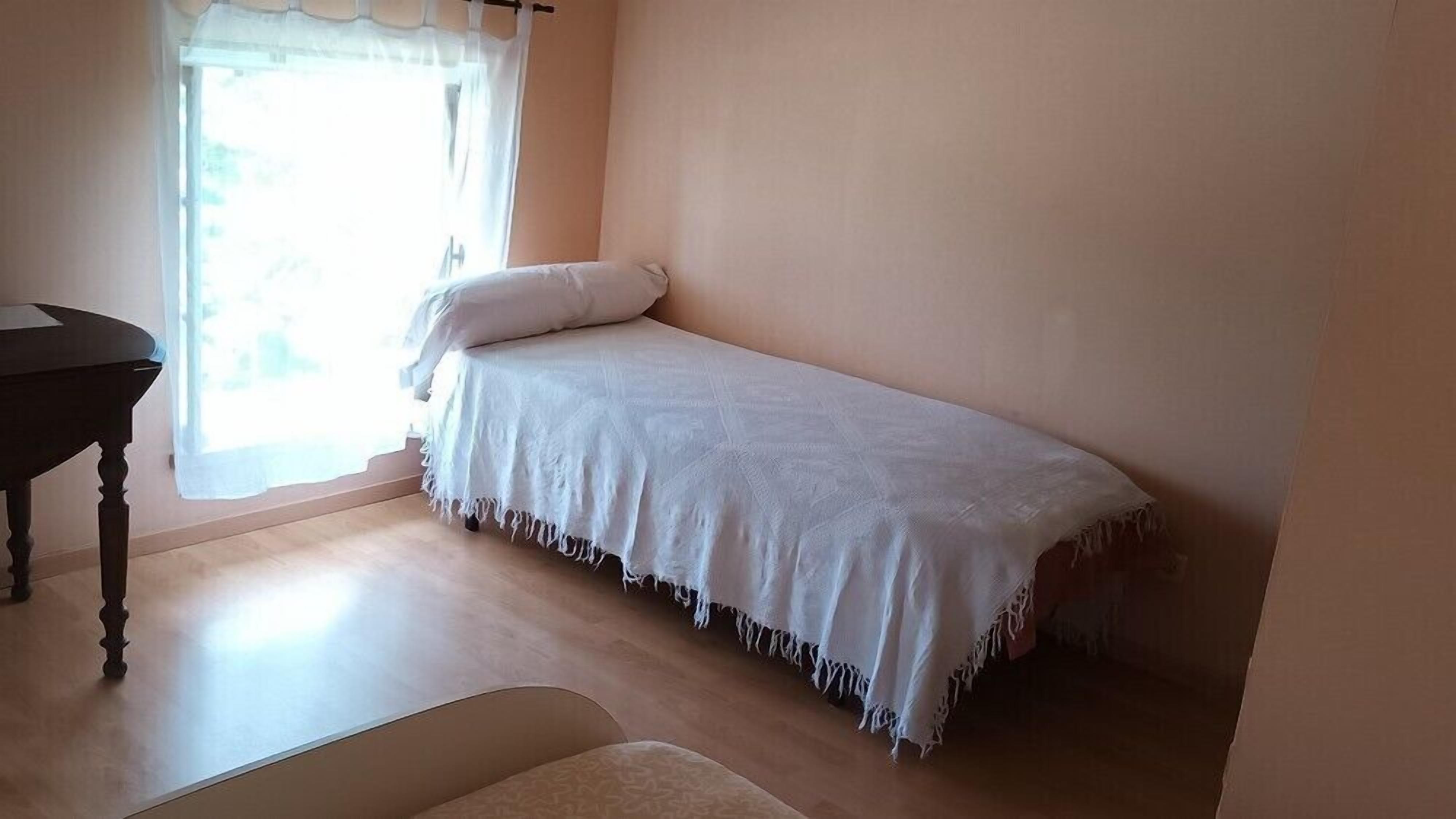 A small, single-bed room with a wooden desk and a chair.